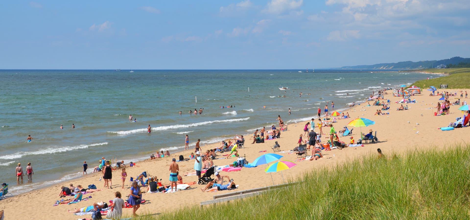 A crowded beach with sunbathers, colorful umbrellas, and people swimming in the water.