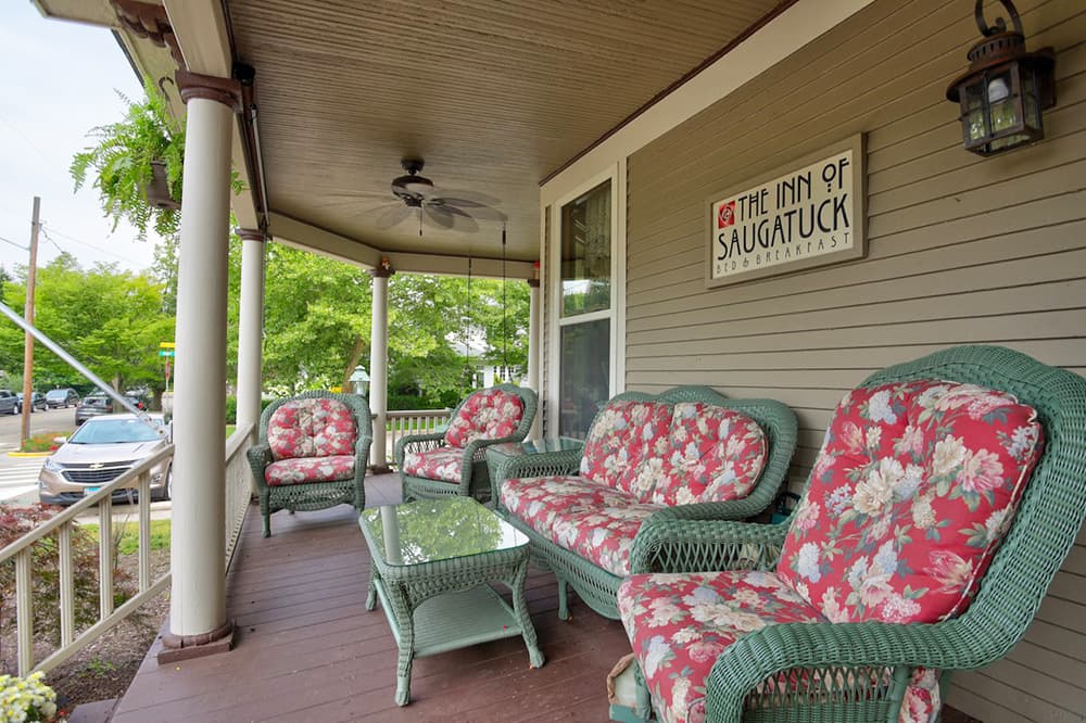 A cozy porch with floral-patterned seating at The Inn of Saugatuck, surrounded by greenery.