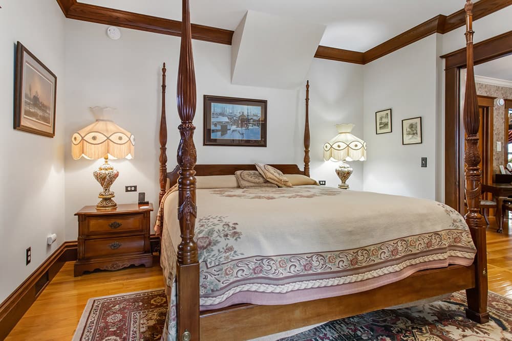 A cozy bedroom with a four-poster bed, decorative lamps, and framed artwork on the walls.