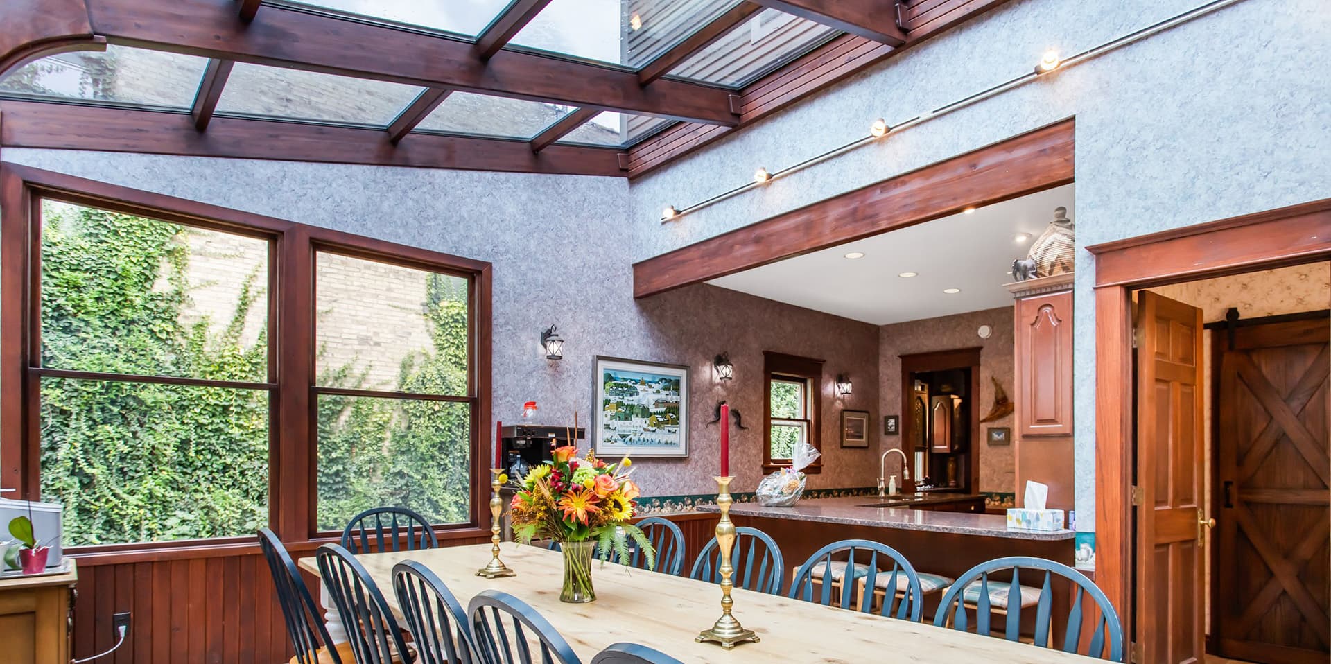 A bright and spacious dining area featuring a wooden table, large windows, and a kitchen in the background.