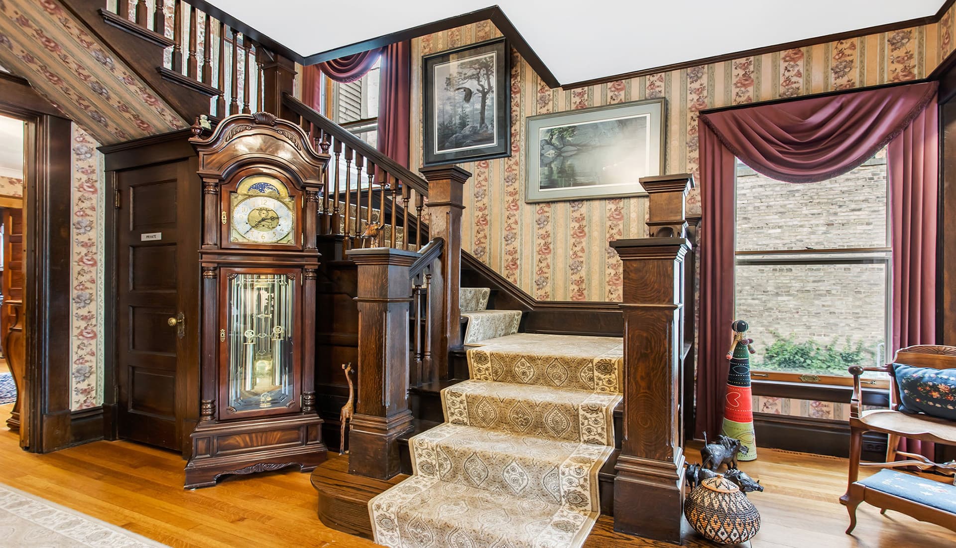 A vintage staircase with ornate woodwork and a decorative wall clock in a charming entryway.