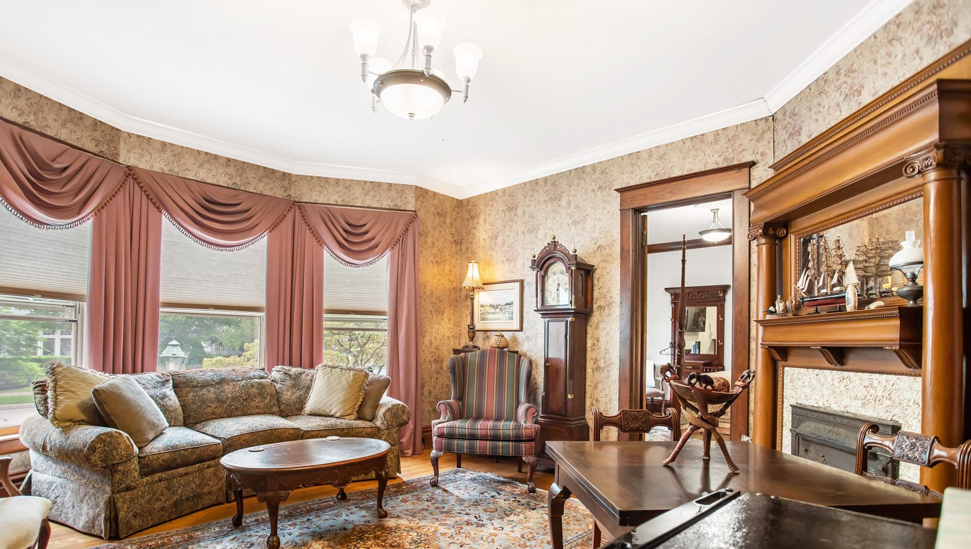 Cozy living room featuring ornate furniture, floral wallpaper, and large windows with drapes.